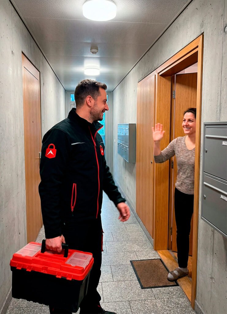 Schlüsseldienst Monteur von Alpine24h begrüßt Kundin im Hausflur in Zürich mit Werkzeugkoffer.